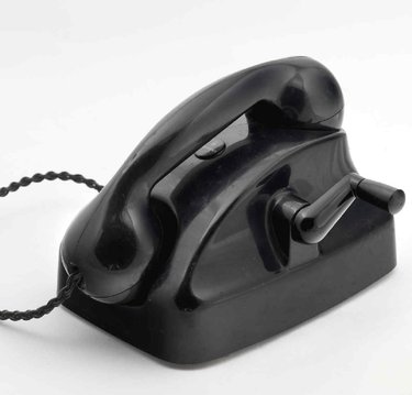 Aparato telefónico de sobremesa de llamada por magneto y batería local, fabricado en plástico negro. El auricular se cuelga en vertical sobre la base.
