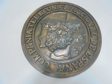 Placa de bronce realizada a molde. Se trata del primer logotipo de la Compañía. Estas placas se colocaban en la entrada de los edificios y centrales de la Compañía Telefónica Nacional de España.